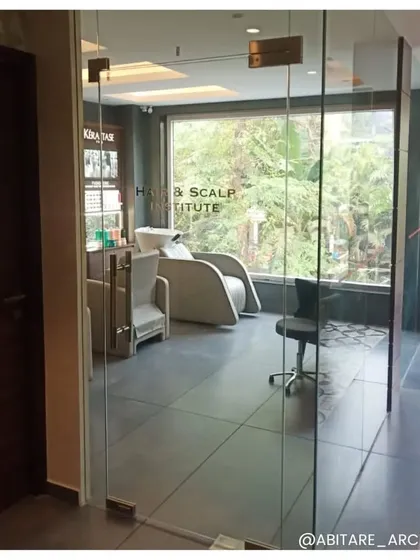 The entrance to the private Hair & Scalp Institute within the salon. The use of glass doors creates a sense of exclusivity while allowing natural light to flow through, with a view of the specialized treatment chairs inside.