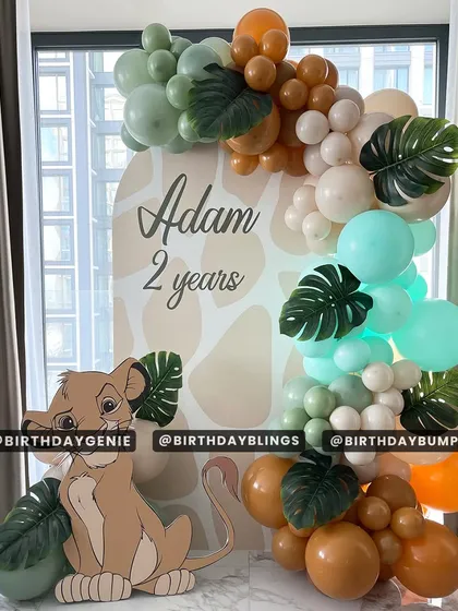 A simple yet sweet Lion King theme for a second birthday, featuring a giraffe-print backdrop and a cute Simba cutout. The balloon colors are a gentle mix of mint, orange, and tan, perfect for a softer look.
