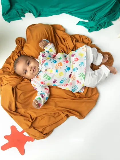 An adorable flat-lay style photo of a baby in a colorful handprint outfit for a Holi-themed shoot.