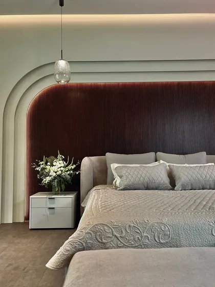 In this bedroom, we created a sanctuary of calm and comfort. A custom-arched, fluted headboard in deep mahogany provides a dramatic backdrop, softened by layered, quilted textiles and a delicate glass pendant light that casts a gentle glow.