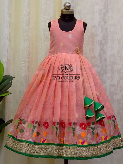 A lovely sleeveless frock in pink organza. The skirt has a colorful border with bird motifs, and the dress is finished with playful green tassels.