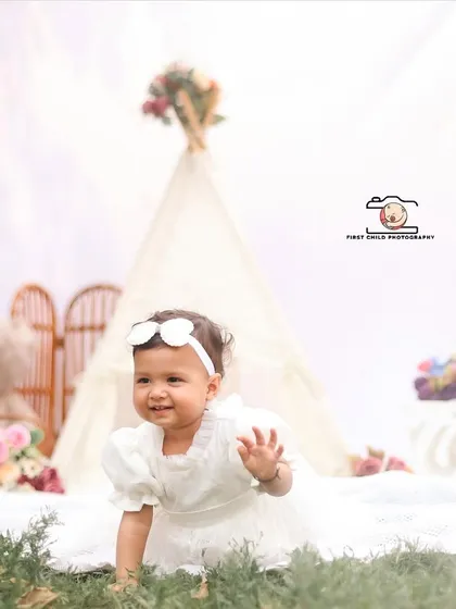 A sweet wave from a happy baby during her outdoor boho photoshoot. Her bright smile and the dreamy white backdrop create a joyful and light filled portrait.
