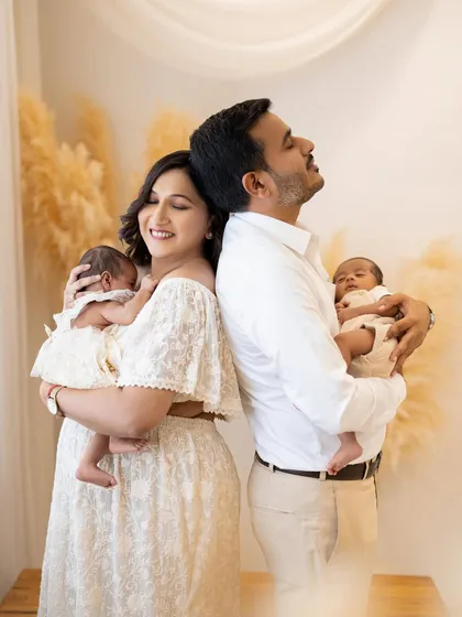 Welcoming newborn twins is double the blessing. In this serene studio portrait, a new mother and father stand back to back, each cradling one of their tiny miracles, capturing a moment of quiet joy and connection.