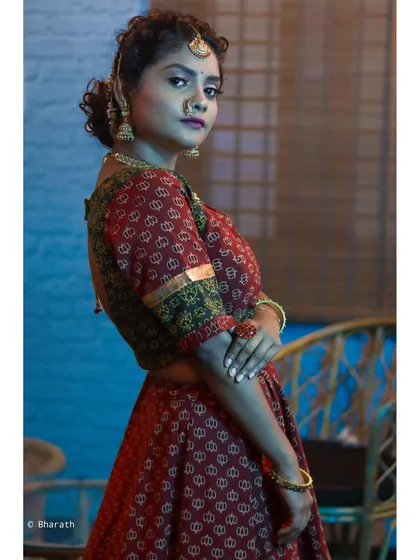 A profile shot of a model in a traditional outfit against a blue and bamboo background. This pose highlights the silhouette of the attire and the elegant hairstyle.