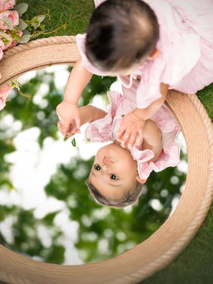 A creative perspective from an outdoor shoot, capturing the baby's reflection as she looks into a rustic mirror on the grass.