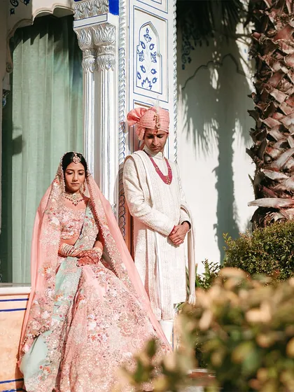 A regal portrait of the couple. The bride is seated while the groom stands, creating a composition that feels both classic and powerful, fitting for a palace wedding.