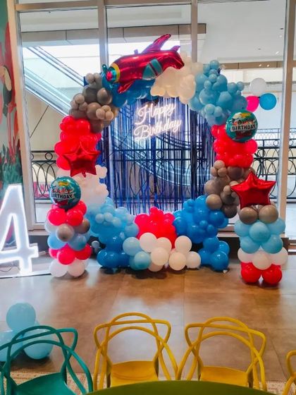 An airplane-themed birthday party for a 4-year-old. This decoration features a circular balloon arch in red, white, and blue, with airplane foil balloons and a blue tinsel backdrop.