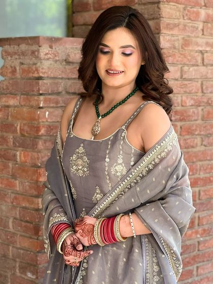 A beautiful daytime party look. The client is wearing a grey suit with a green necklace, and her makeup is fresh and natural.