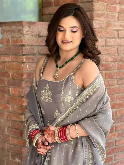 A beautiful daytime party look. The client is wearing a grey suit with a green necklace, and her makeup is fresh and natural.