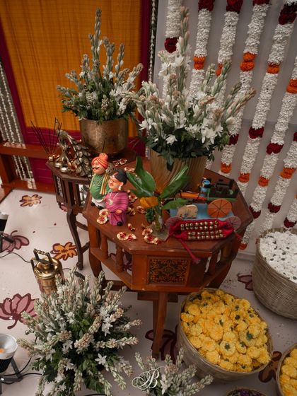 An overhead view of the antique tables on the main stage, adorned with Channapatna dolls, fresh tuberose, and baskets of marigolds. Every element is carefully placed to create a rich, layered, and visually interesting setup.