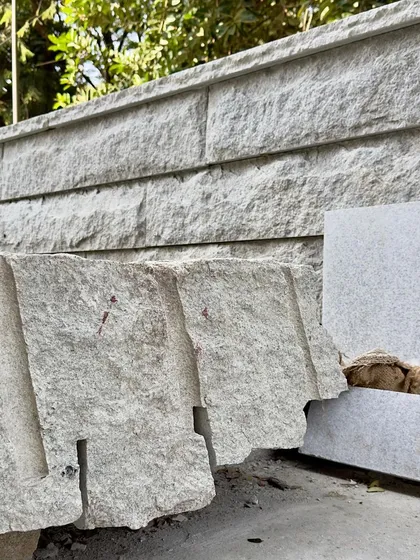 Discarded, broken pieces of stone next to a newly built wall, showing the process of selection and craft.