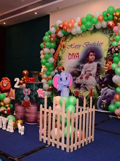I bring the jungle to your party with this safari-themed setup. It features a personalized backdrop with the birthday child's photo, a green and orange balloon arch, and fun cutouts of jungle animals like lions and elephants.