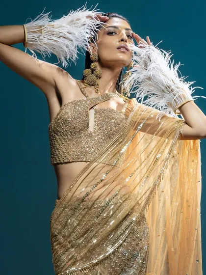 A striking shot for Kavita Arora Couture, this image features a model in a golden sequin sari-gown, accented with dramatic white feather cuffs. The styling creates a fusion of classic glamour and avant-garde texture.