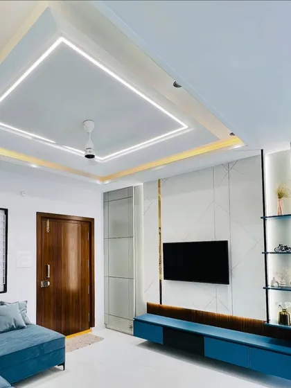 This living room TV unit features a dark blue floating console against a white paneled wall with geometric patterns. The design includes open, backlit shelving for a modern and functional display.