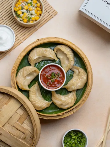 A different angle of our steamed momos, highlighting the perfect half-moon shape and the vibrant red of our house-made chutney.