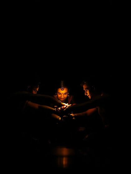 The 'Nagamandala' flame scene, almost completely in shadow. This minimalist lighting creates a sense of mystery and focuses all attention on the symbolic flame.