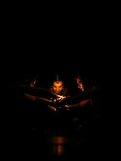 The 'Nagamandala' flame scene, almost completely in shadow. This minimalist lighting creates a sense of mystery and focuses all attention on the symbolic flame.