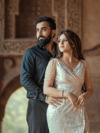 A glamorous couple portrait set against the textured stone walls of an old fort. The contrast between the modern, elegant attire and the ancient backdrop creates a striking visual.