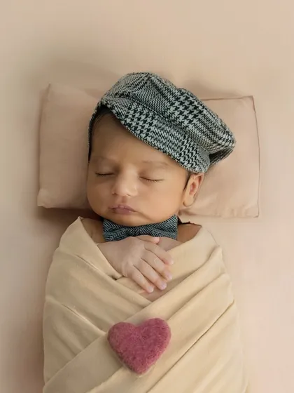 This little gentleman, complete with a dapper cap and bowtie, is already stealing hearts. Even in sleep, his personality shines through in this styled newborn portrait.