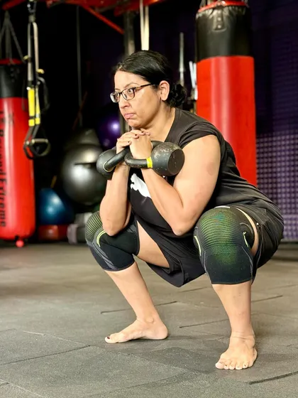 A member performs a kettlebell goblet squat, an excellent exercise for building lower body strength and improving core stability. Her focused expression shows her dedication.