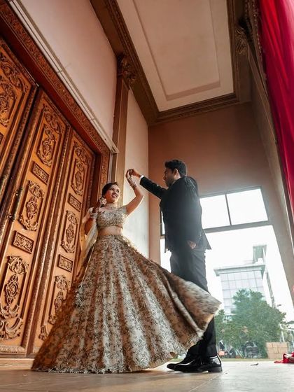 A wide-angle shot of the couple dancing, capturing the full sweep of the bride's lehenga against the grand venue.