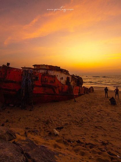 A shipwrecked boat on Padubidri beach at sunset. The scene is both beautiful and melancholic, telling a story of a journey's end.