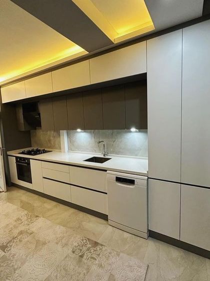 This wide shot shows the entire length of the galley kitchen, including the tall pantry unit at the end. The combination of recessed ceiling lights and under-cabinet LEDs ensures the kitchen is bright and functional at all hours.