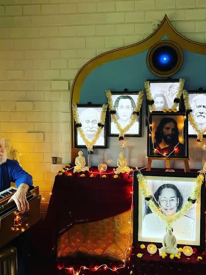 Nayaswami Haridas at the harmonium, chanting before the beautifully lit altar of our masters. The atmosphere is filled with sacredness and devotion.