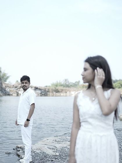 An artistic shot with the bride in the foreground and the groom in the background, both looking in different directions by a lake.
