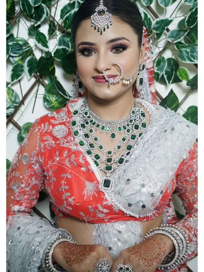 A bride wearing a layered American Diamond and emerald necklace with a red and silver lehenga. This set is perfect for making a bold statement.
