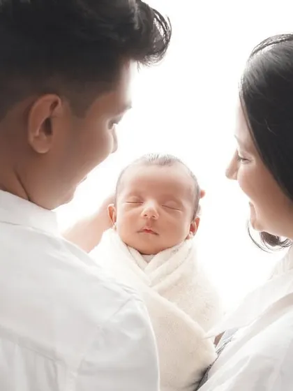A beautiful shot from behind the parents, focusing on the newborn sleeping peacefully in their arms. This perspective emphasizes the feeling of protection, love, and wonder.