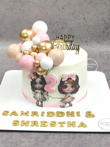 An adorable cake for twin girls turning two. The design features two cute characters holding a balloon garland.
