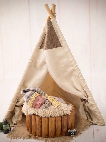 A cozy camping theme, with a newborn sleeping in front of a miniature teepee, complete with a tiny camera and lantern for a touch of adventure.