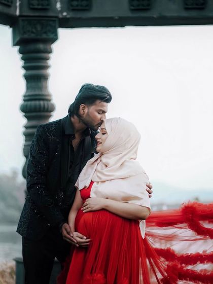 An intimate moment between partners, celebrating the new life they've created. The flowing red tulle gown and his patterned black blazer create a look that is both romantic and sophisticated for their maternity session.
