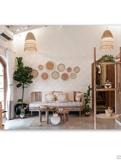 A bright and airy living room in a Goan villa, with light wood furniture, woven lampshades, and a wall decorated with wicker plates. The aesthetic is rustic, coastal, and effortlessly chic.