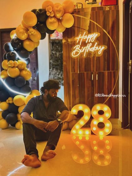 A client enjoying his birthday setup at home, featuring a hoop backdrop with a black and yellow balloon garland and a neon sign.