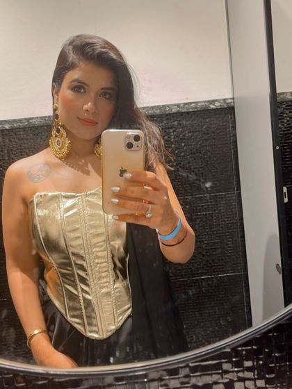 My client captures a mirror selfie, giving a full view of how these large, traditional gold-tone earrings complete her modern fusion look with a gold corset top.