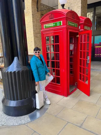 Leaning against a pillar next to the red phone booths in London, creating a more relaxed and candid feel.