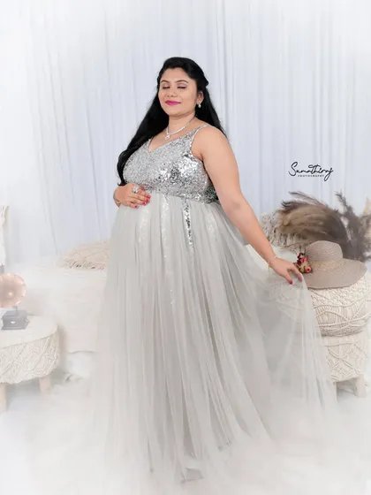 A serene portrait of a mother-to-be in a silver and white gown. The boho-chic setup with macrame and pampas grass creates a soft, dreamy, and stylish atmosphere.