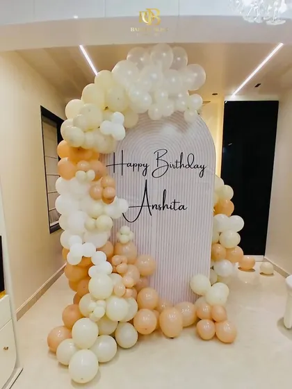 Soft and elegant decor for a personalized birthday celebration. This setup features a beautiful arch backdrop with the birthday person's name and a gentle cascade of pastel and cream-colored balloons.