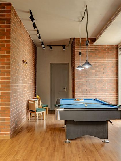 This contemporary entertainment space features beautiful red brick walls and a concrete-finished ceiling. A pool table and modern track lighting create a relaxed, industrial vibe.