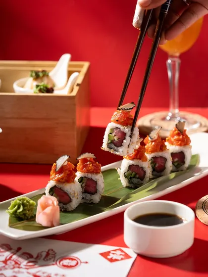 Spicy tuna sushi rolls on a long platter. The hand holding one with chopsticks adds action and makes the viewer imagine taking a bite.