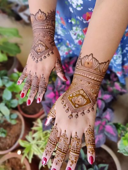 This back-hand design features a diamond-shaped frame with a lotus inside. The pattern extends into a wristband, or cuff, and is complemented by delicate jhumka-like drops.