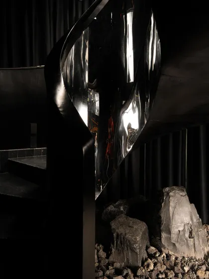 The sculptural staircase, seen from a different angle, its metallic sheen a stark contrast to the surrounding darkness.