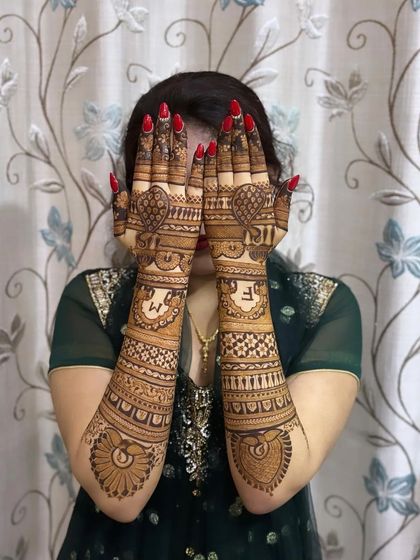 A full bridal mehandi with initials "M" and "F" on the palms. The design extends up the arms with traditional patterns, perfect for a bride.