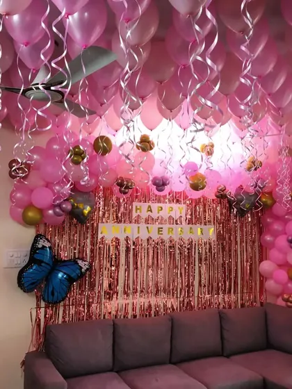 An elaborate anniversary decoration with a ceiling full of pink balloons. The setup includes a pink foil curtain and a balloon arch over the sofa.