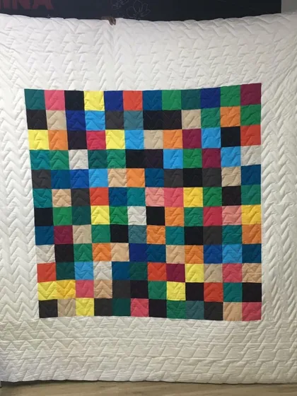 A colorful pixelated quilt with a wide, white border featuring herringbone quilting.