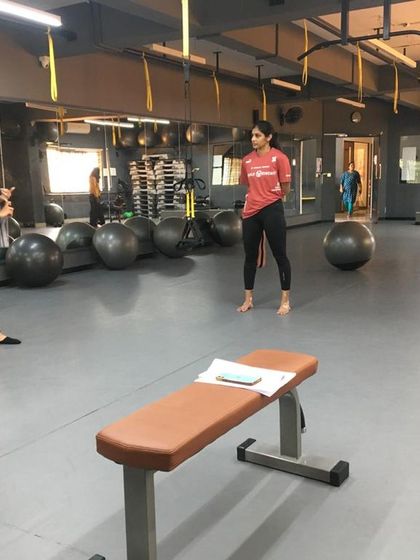 A female master trainer leads a practical session, instructing students on exercise form and theory in a gym setting.