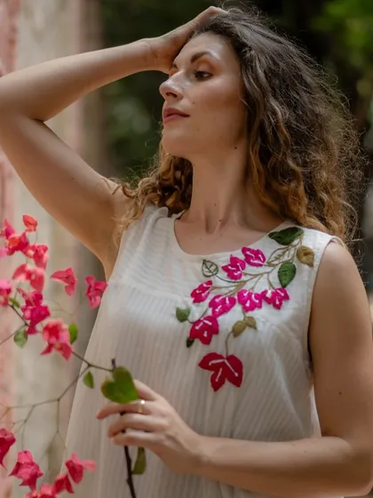 A model wears a beautiful sleeveless top with delicate bougainvillea embroidery, a perfect example of wearable art.