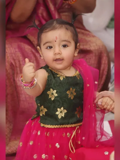 An adorable baby girl in a traditional lehenga gives a thumbs-up to the camera. We love capturing these cute and spontaneous gestures.